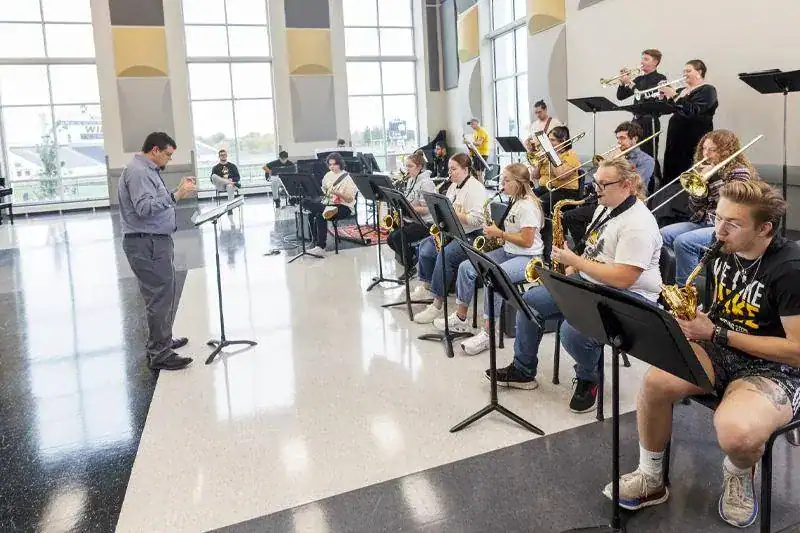 Estudiantes tocando instrumentos de viento metal y viento madera durante un ensayo de banda dirigido por un director en Wayne State College Nebraska.